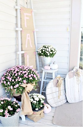 Beautiful Fall porch decor with pink and white flowers, a Fall banner in buralp with pink painted letters, and two large neutral colored DIY wood pumpkins.