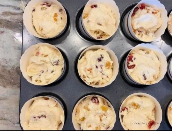 A muffin tin filled with paper panettone cups that are filled with equal amounts of panettone muffin batter.