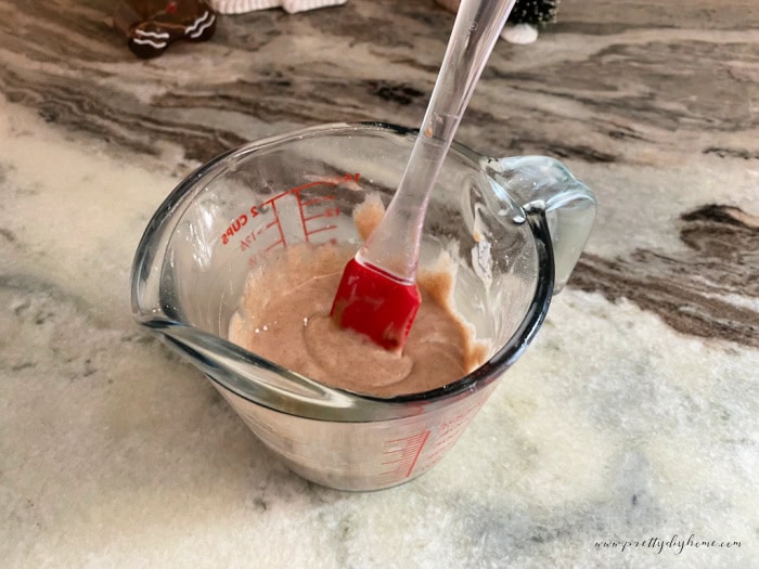 A measuring cup filled with cinnamon flavored glaze for gingerbread scones.