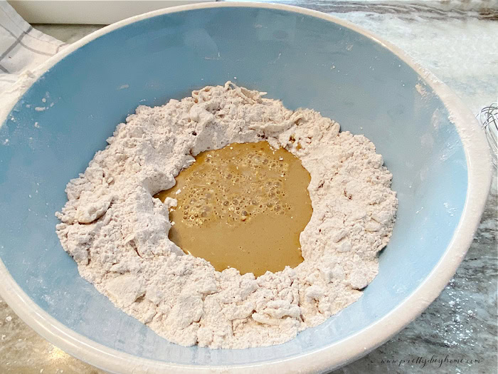 A large mixing bowl filled with the dry ingredients for gingerbread scones.  There is a well in the middle of the dry ingredients where the wet molasses ingredients are.