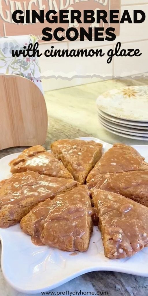 A tray of gingerbread scones sitting on a white snowflake platter.. The golden brown scones are glozzy because of a cinnamon glaze topping.