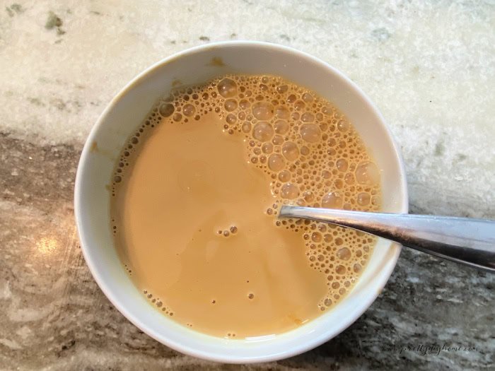 A small white mixing bowl filled with molasses, cream and brown sugar, its all mixed into a creamy golden mixture. Wet ingredients for making gingerbread scones.