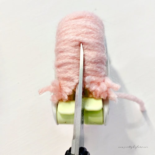 A view from the side of a pom pom maker, that shows the scissors placement cutting the yarn into cute bits for pom poms.