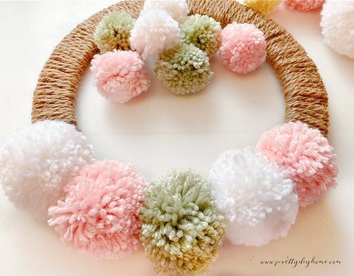 A diy Easter wreath with pom poms.  The image shows the first layer of pom poms being place along the edge to cover a bald spot on the wreath form.