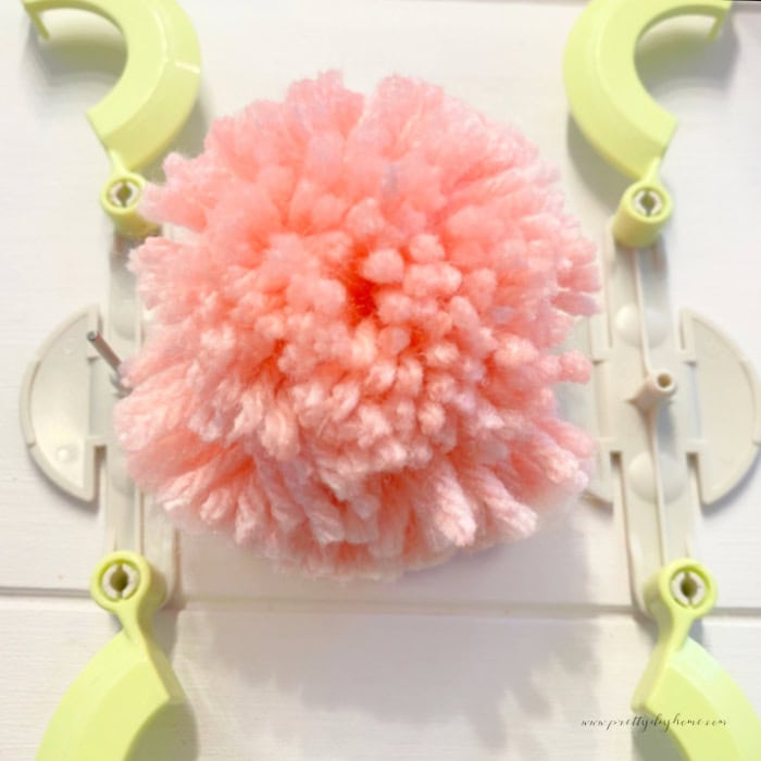 A finished pink pom pom laying inside the two halves of a pom pom maker.  