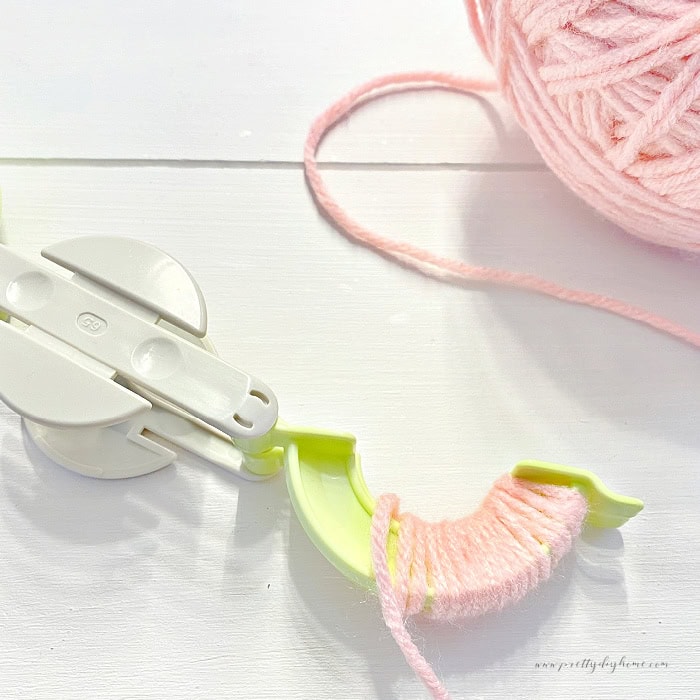 Wrapping pink yarn onto a green arm of a pom pom maker