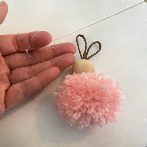 Attaching fishing wire to hang a DIY Pom Pom Easter Bunny craft.