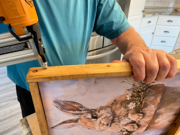 A man with an air nailer attaching the side of a wood frame to a bunny print canvas