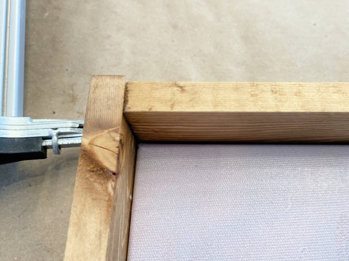 A close up of the corner on a DIY wood frame.  The image shows the overlap of the wood, and an air nailer attaching the two pieces together for stability.