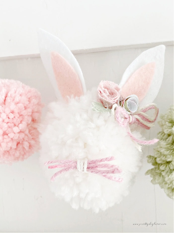 A close up of Easter bunny pom pom, that is hung with smaller pom poms in pastel pink and green on each side.