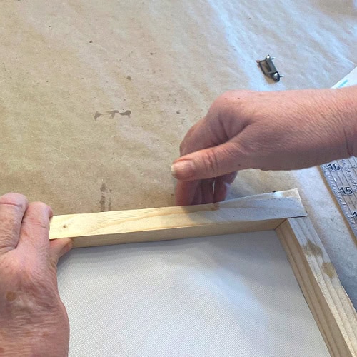 Folding the top edge of a canvas over to adhere to a wood backframe