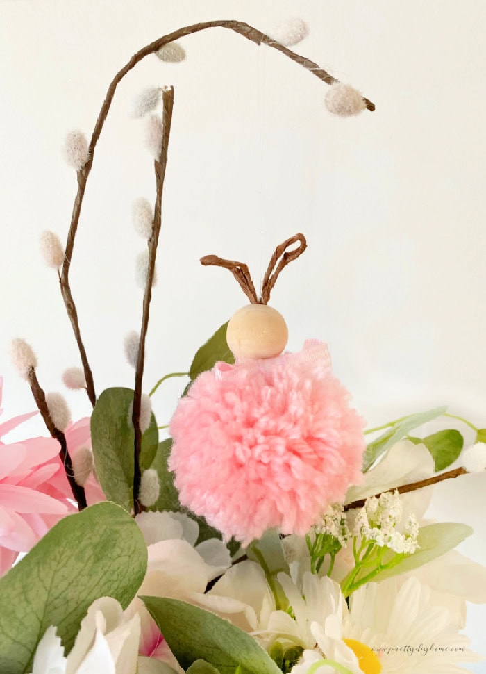 A pink DIY pom pom bunny suspended from a pussy willow branch as part of an Easter flower arrangement.