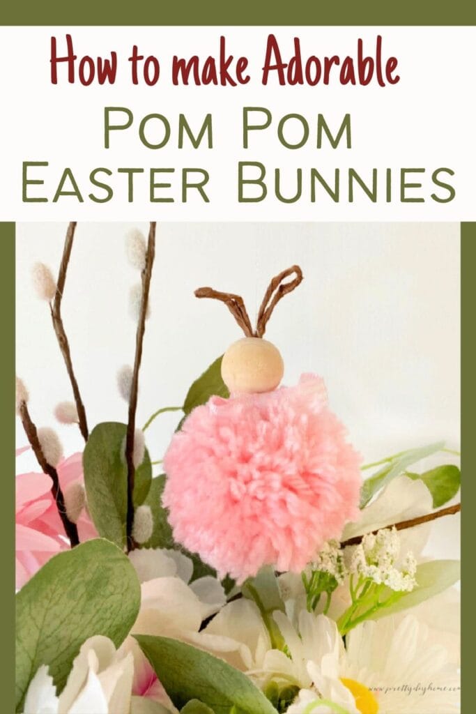 A pretty pom pom bunny in pink hanging from  a pussy willow branch aspart of a flower arrangement for Easter.  The flowers are white and pink with soft green leaves.  There is overlay text that says How to Make Adorable Pom Pom Easter Bunnies.