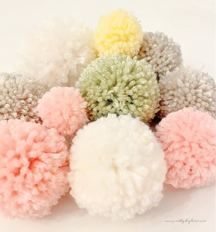 A large stack of cute fluffy pom poms in bright spring pastels.  The pom poms are being used to make an Easter bunny garland.