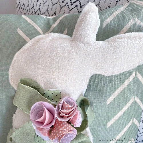 Handmade rolled fabric flowers are embellishing a white fabric easter bunny.