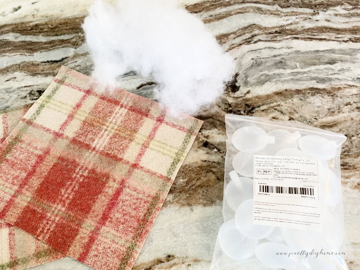 A picture of 3 materials you need to make a DIY dog toy that squeaks. A square of heavy scrap fabric, some dollar store fluffing and a bag of dog squeakers you can buy online.