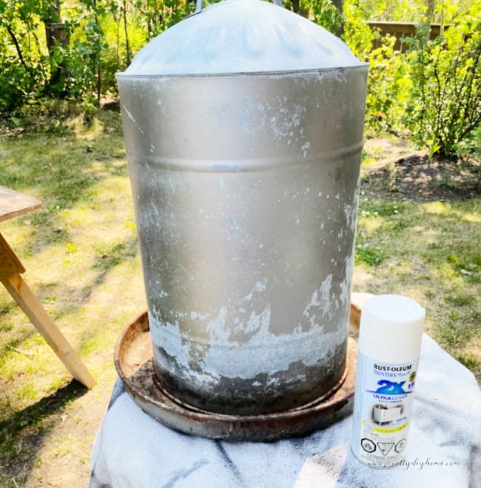 A large damaged chicken feeder before image. The feeder is miscolored and old and there is a can of cream colored rustoleum outdoor spray paint beside it.
