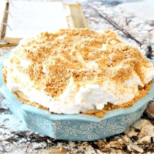 A large and fluffy flapper pie recipe served in a blue ceramic pie plate. You can see the graham cracker crust, thick layer of meringue and the graham cracker crumb topping.