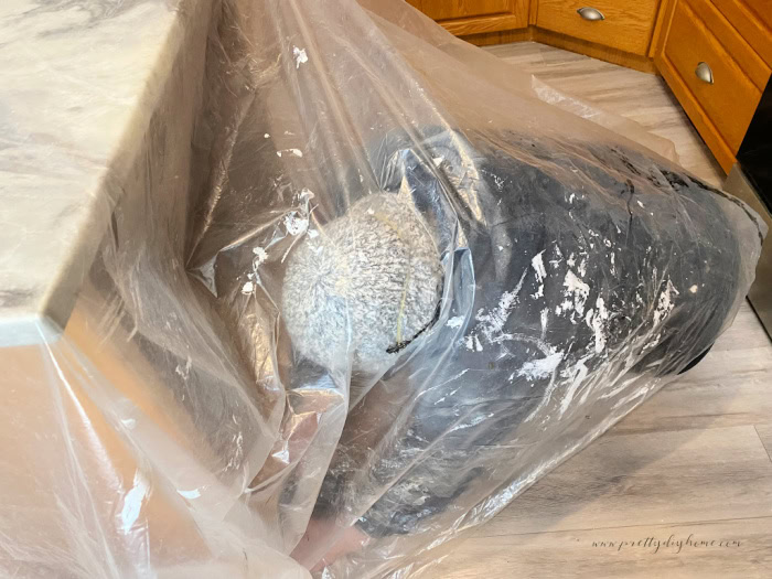Sanding llower kitchen cabinets on an island. The person sanding is working under a sheet of plastic to prevent dust.
