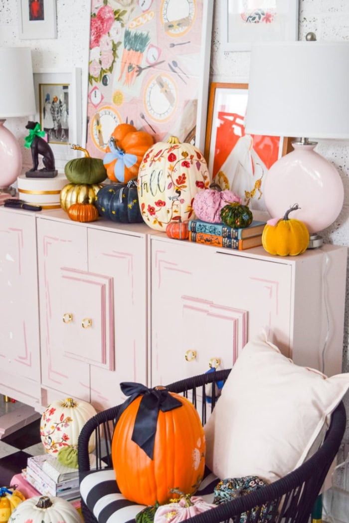 A pink buffet decorated with assorted colorful painted pumpkins in different patterns.