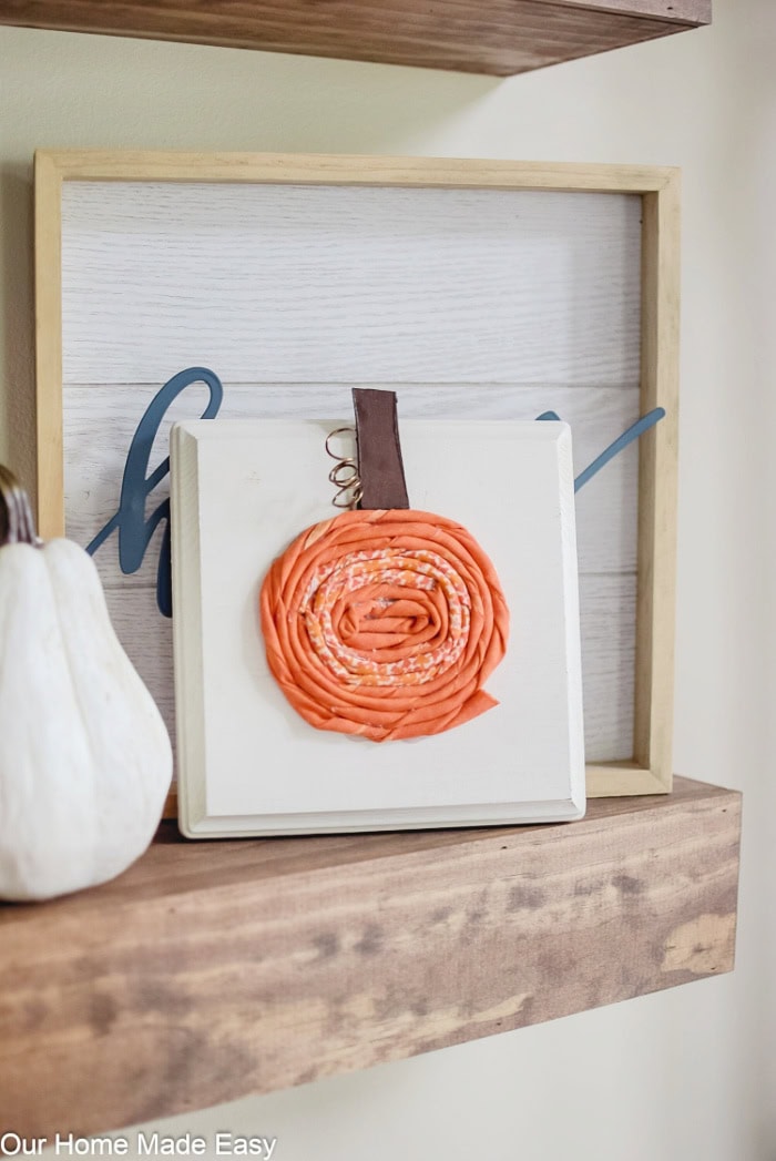 A fabric pumpkin made inti the front of a wooden board for diy pumpkin wall art.