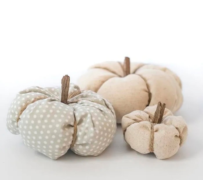 Three neutral coloredd fabric pumpkins.  One is large and cream one is polka dotted and the third one is a small pumpkin in cream.  The background is solid white.
