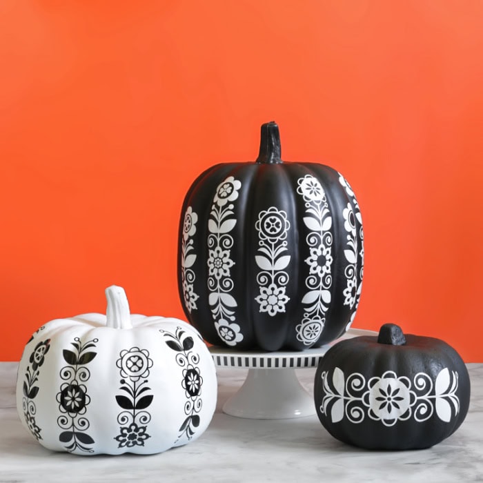 Three black and white painted pumpkins each one decorated with coordinating vinyl patterns.