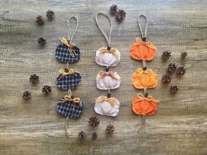 Three pumpkin door handers made using fabric and twine. The first one is black plaid, then a cream and finally orange pumpkin hangers. Each pumpkin has a pretty bow in it made with raffia and yarn.