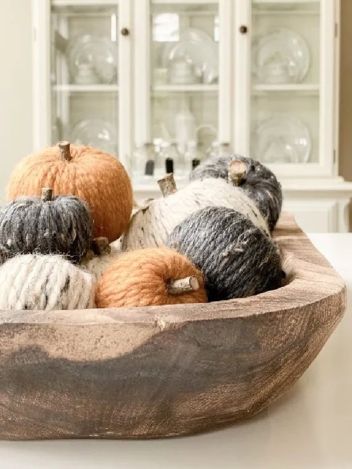 A stack of adorable wool wrapped pumpkins in orange, grey cream or cream colors.  The wool wrapped pumpkins are displaued in a large dough bowl for 
Fall decor