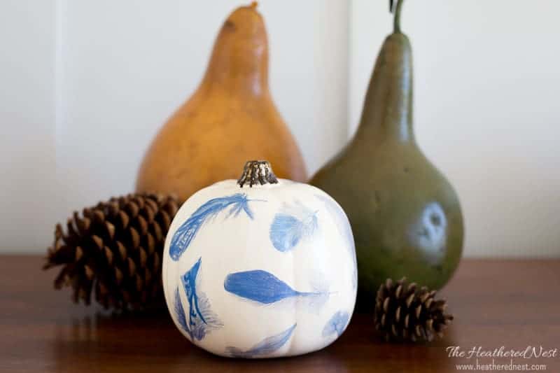 A blue and white pumpkin decorated with blue feather tattoo paper.  There is an orange and a green gourd in the background.