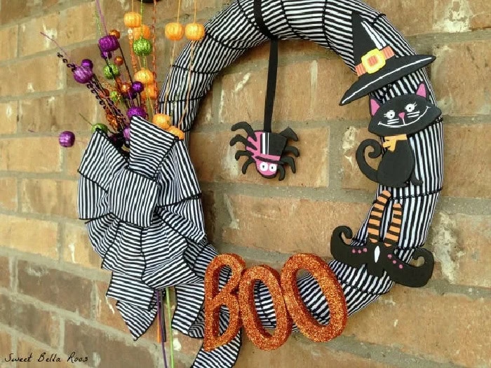 A striped ribbon wrapped Halloween wreath featuring a black cat.