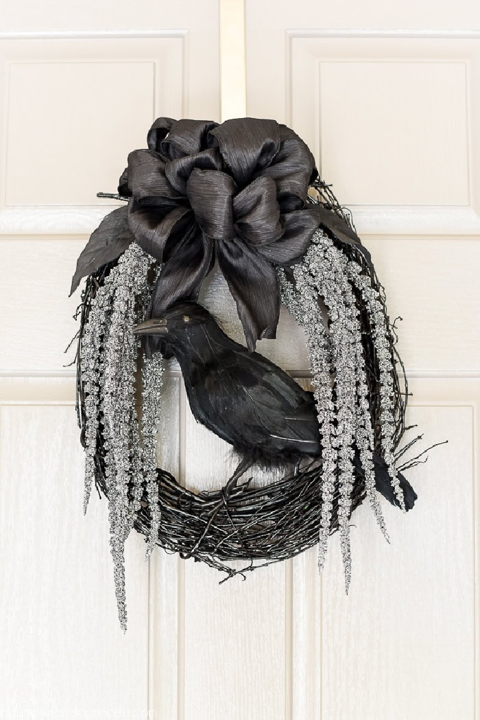 A very elegant black crow Halloween wreath.  The wreath is all black with an elegant black bow on the top, and long grey florals hanging down the side.  Very mournful looking.