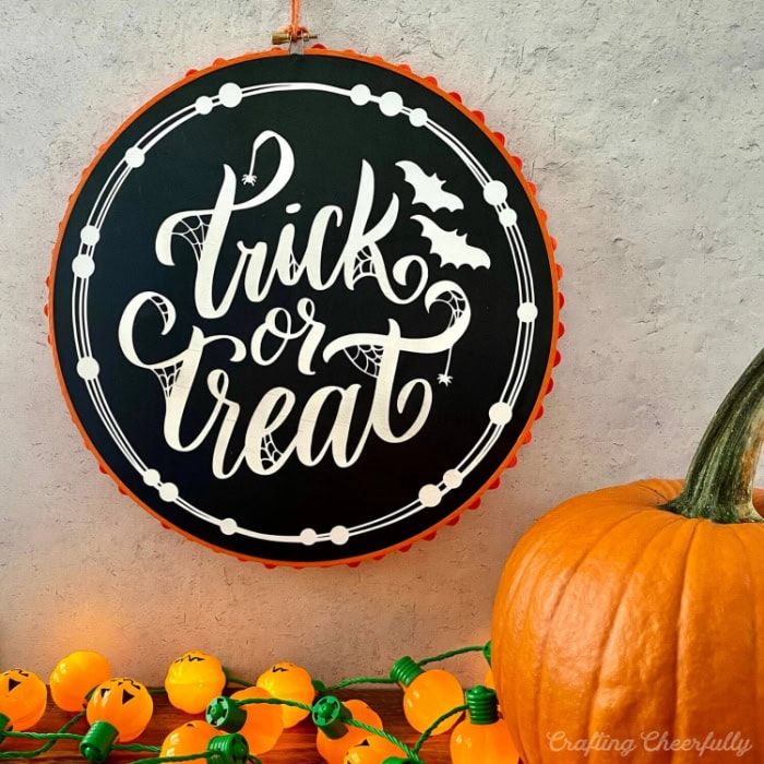A round hoop painted orange enclosed a black and white wreath that says trick or treat.