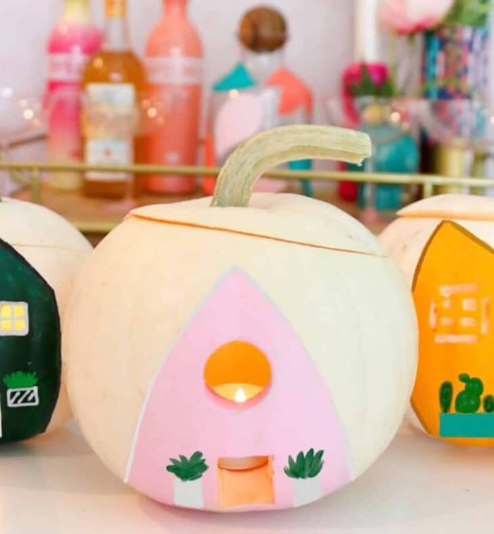 Three cheerfully colored cream pumpkins painted with cheerful pink, orange and black playhouses on the front.  The pumpkins are hollowed and you can see a candle inside.