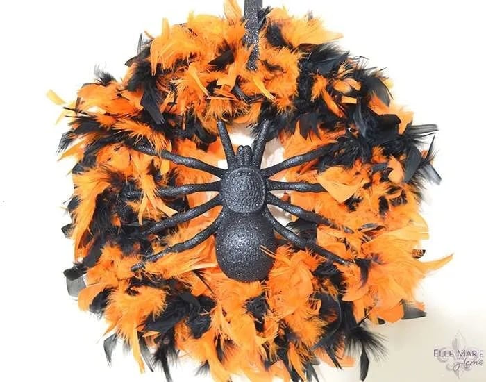 A DIY Halloween wreath made with an orange and black feathered boa background and centered with a large plastic black spider.
