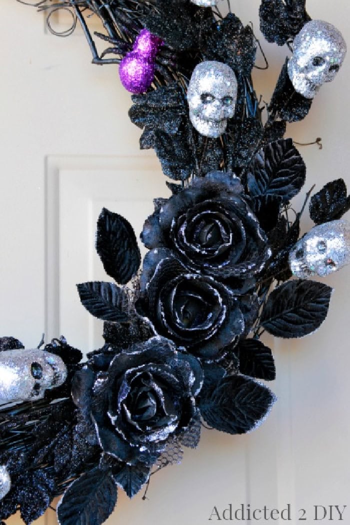 A closeup of the embellisments on a all black DIY Halloween wreath.  You can seree a sparkling silver mini skull a cute purple sparkling spider and three very elegant blak roses.