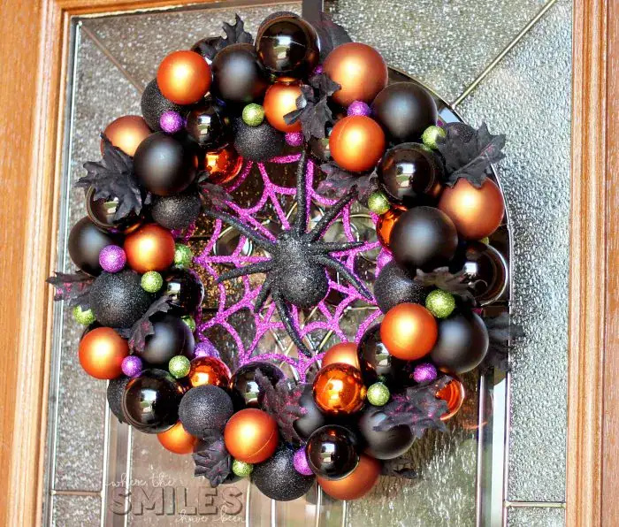 A large Halloween wreath hanging on a front door.  The wreath is encircled with black and orange ornaments and centered with a large black spider.