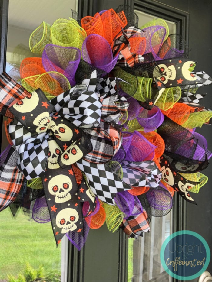 A very brght and cheerful homemade wreath made with assorted curlu ribbons hanging on a front door for Halloween.