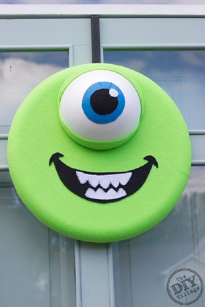 A btrightly colored green monster DIY Halloween wreath, with a single large eye and big smiling face.