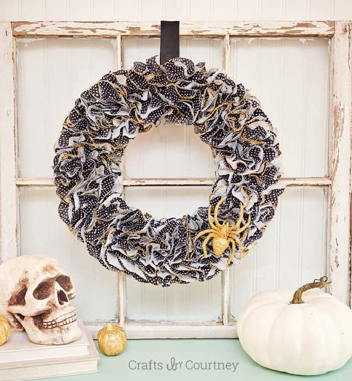 A large fluffy Halloween wrrath made with black and white cupcake wrappers.  There is a gold sparkling spider in the lower corner, and the wreath is hanging from a window frame.