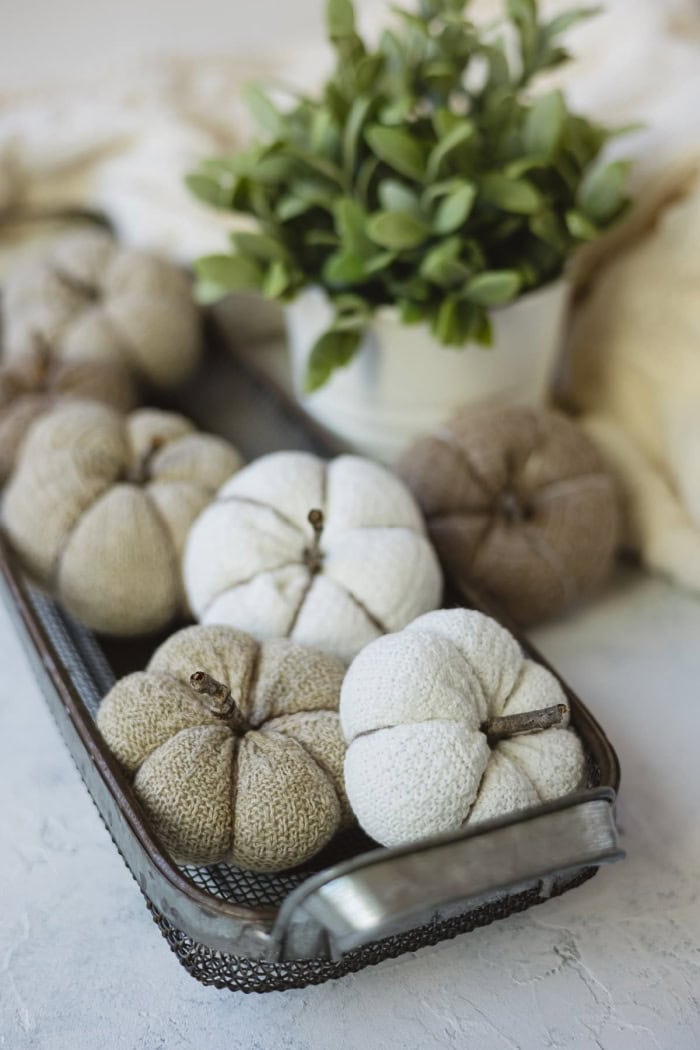 A galvanized basket filled with several adorable homemade pumpkin decorations for fall. The DIY pumpkins are cream or white.