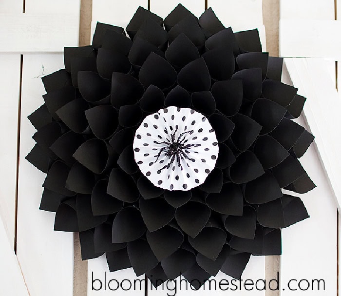 A homemade Halloween wreath with a large flower shape around the outside in black the center is black and white and features a creeph plastic black spider.