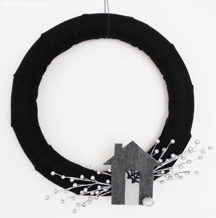 A plain black Halloween wreath thats elegant and simplistic.  It feature a black base, with a grey haunted house and white berry embellishments.
