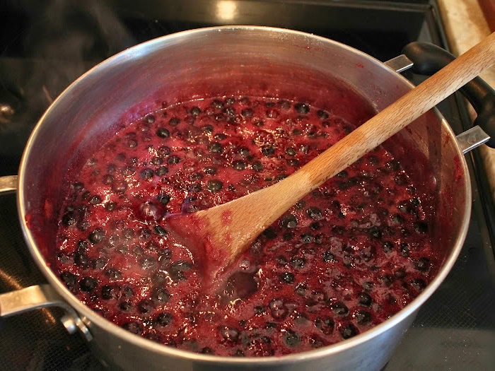 A large pot filled with hot saskatoon jam thats cooling. You can see pink foam impurities on the top.