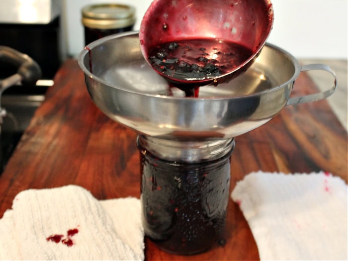 A jam or jelly jar fit with a canning funnel. The jar is being filled with hot fresh saskatoon jam.