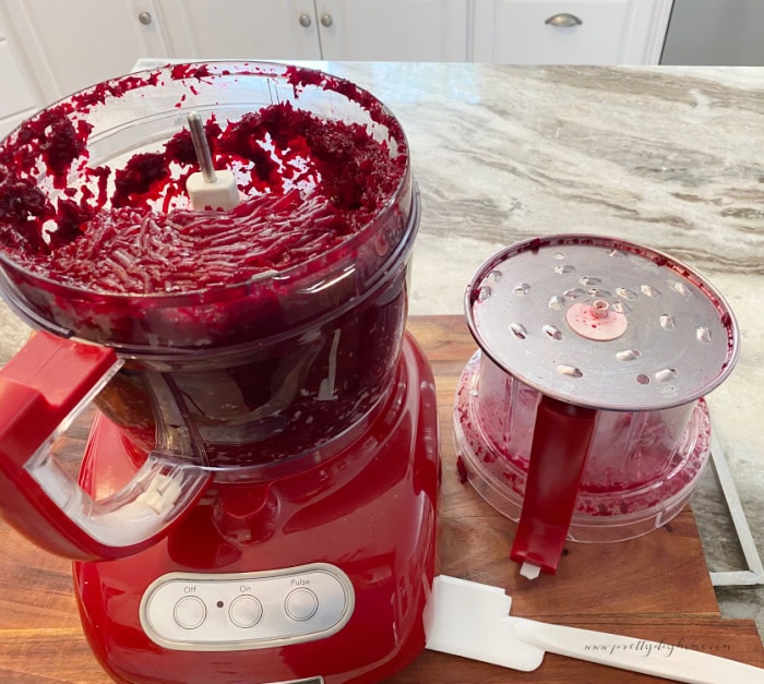 Grating fresh cooked beets in a large food processor.  You can see the grated beets inside the bowl as well as the grater used.