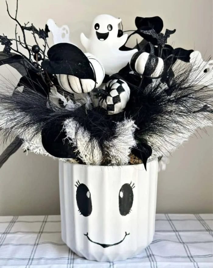 An all black and white Halloween arrangement with a centerpiece thats a white bucket with a cute ghost face on it.