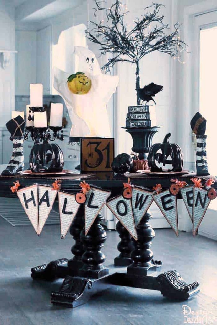 A ghost themed Halloween tablescape feautring a large ghost, black pumpkins, crows and a banner that says Halloween.