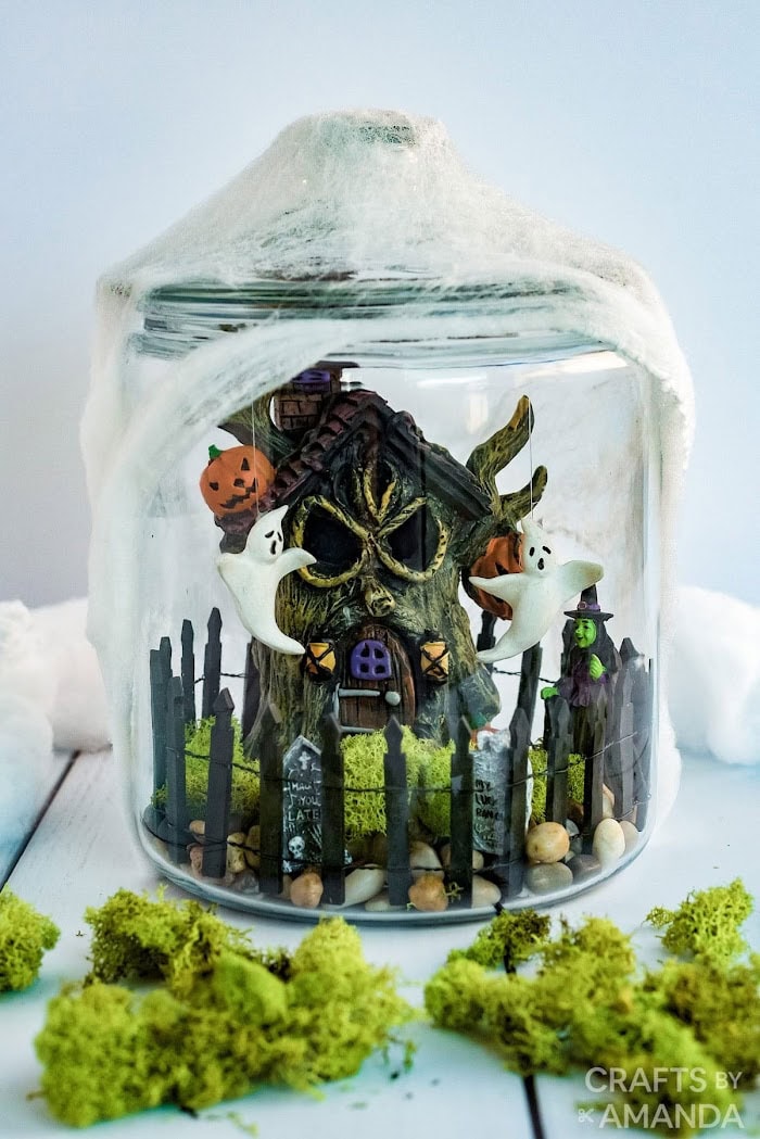 A Halloween table terrarium centerpiece featuring a witch in her yard with green moss and a fun witch's hut.