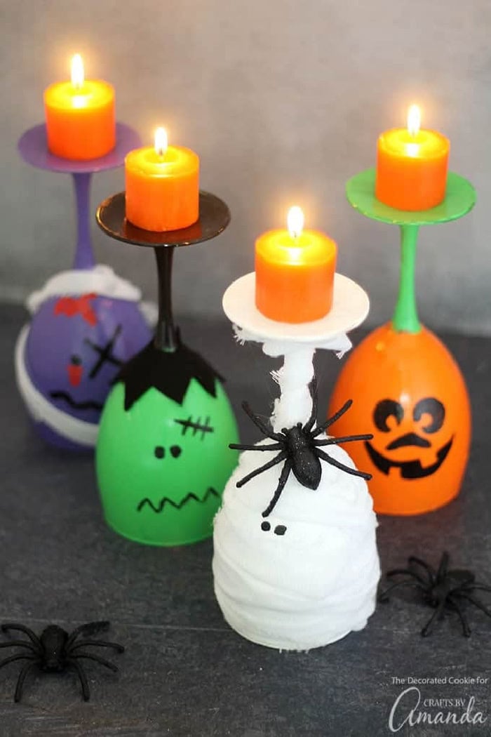 Four colorful and fun Halloween themed wine glasses a ghost, pumpkin frankenstein and a witch.  The wine glasses are flipped over holding a candle.